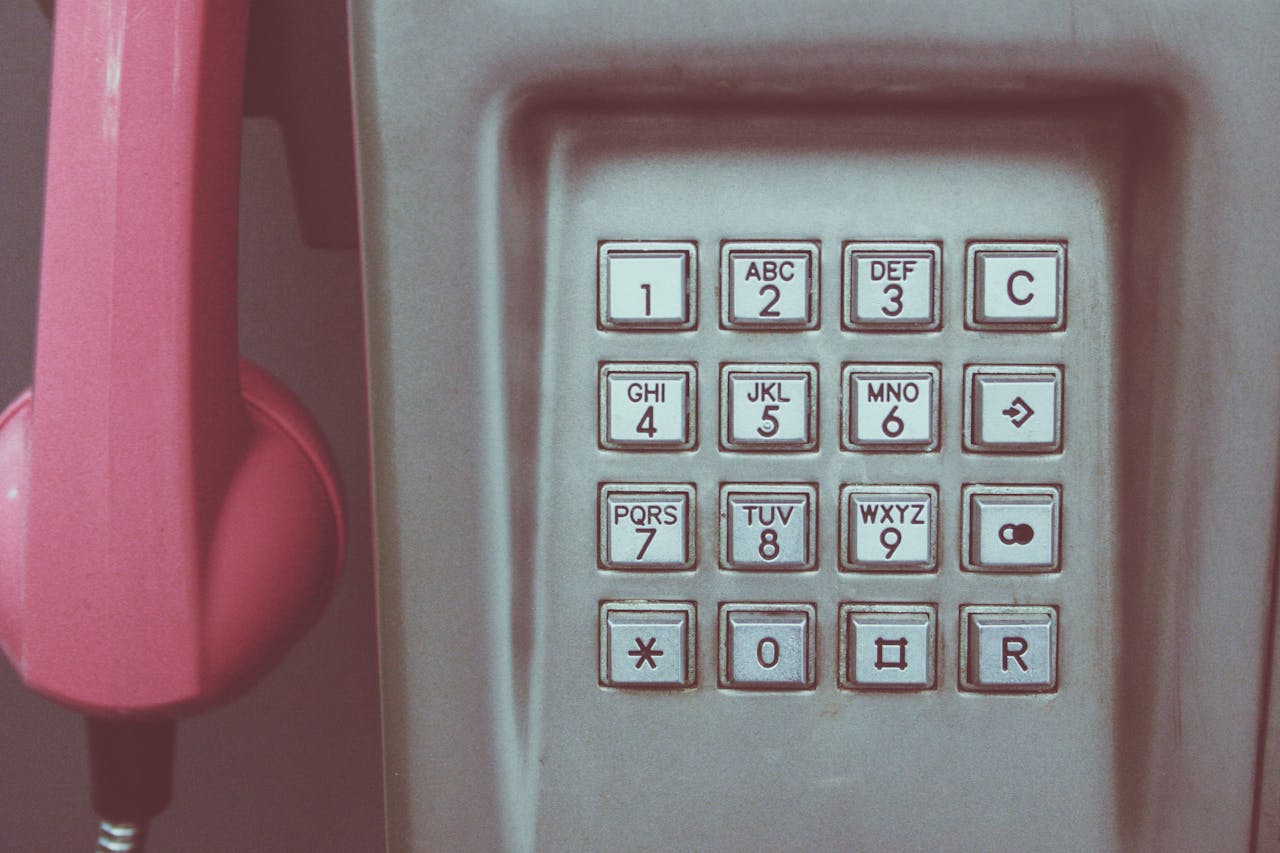 Close-up of a vintage payphone keypad with pink receiver, highlighting retro technology.