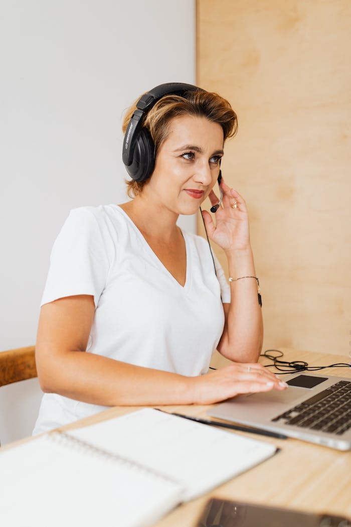 A woman in headphones works at a laptop in a modern office setting.